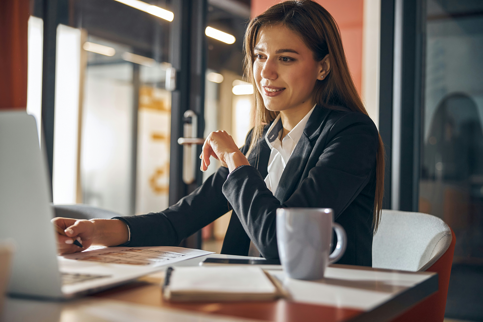 Business-Frau sitzt an Schreibtisch und blickt in Laptop mit Salesforce Experience Cloud.