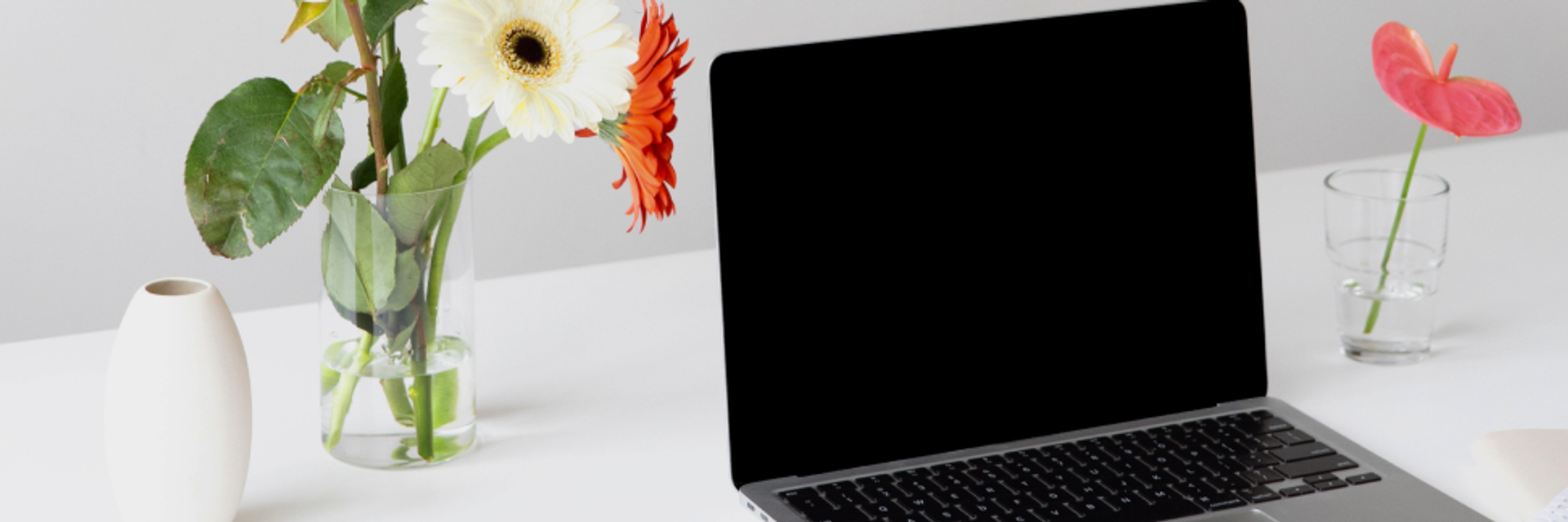 Ein Laptop und daneben eine Vase mit Gerbera.