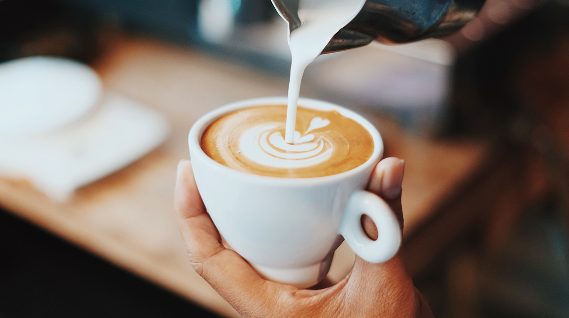 Milch wird in einen Cappuccino gegossen.