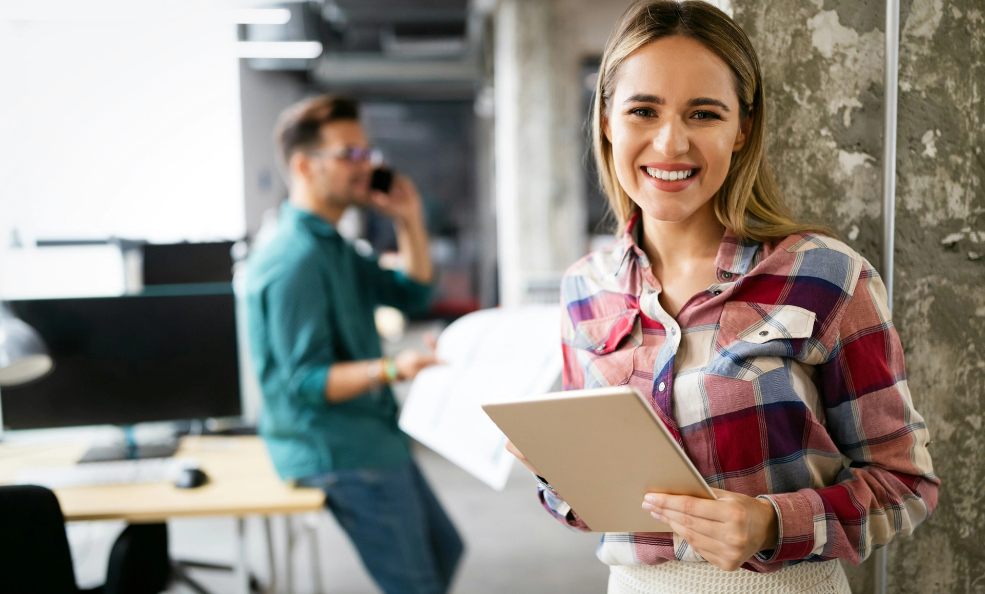 Woman wearing a plaid shirt holds a tablet with Agentforce Marketing in her hands and looks at the camera.