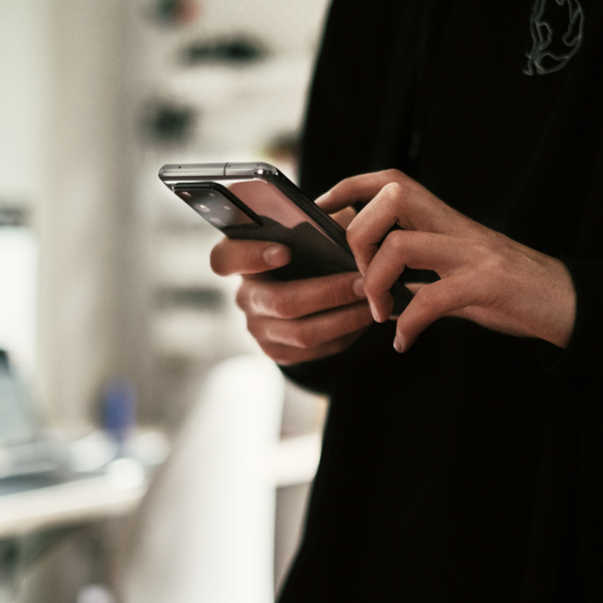Person mit schwarzem Pullover hält ein Smartphone vor sich.