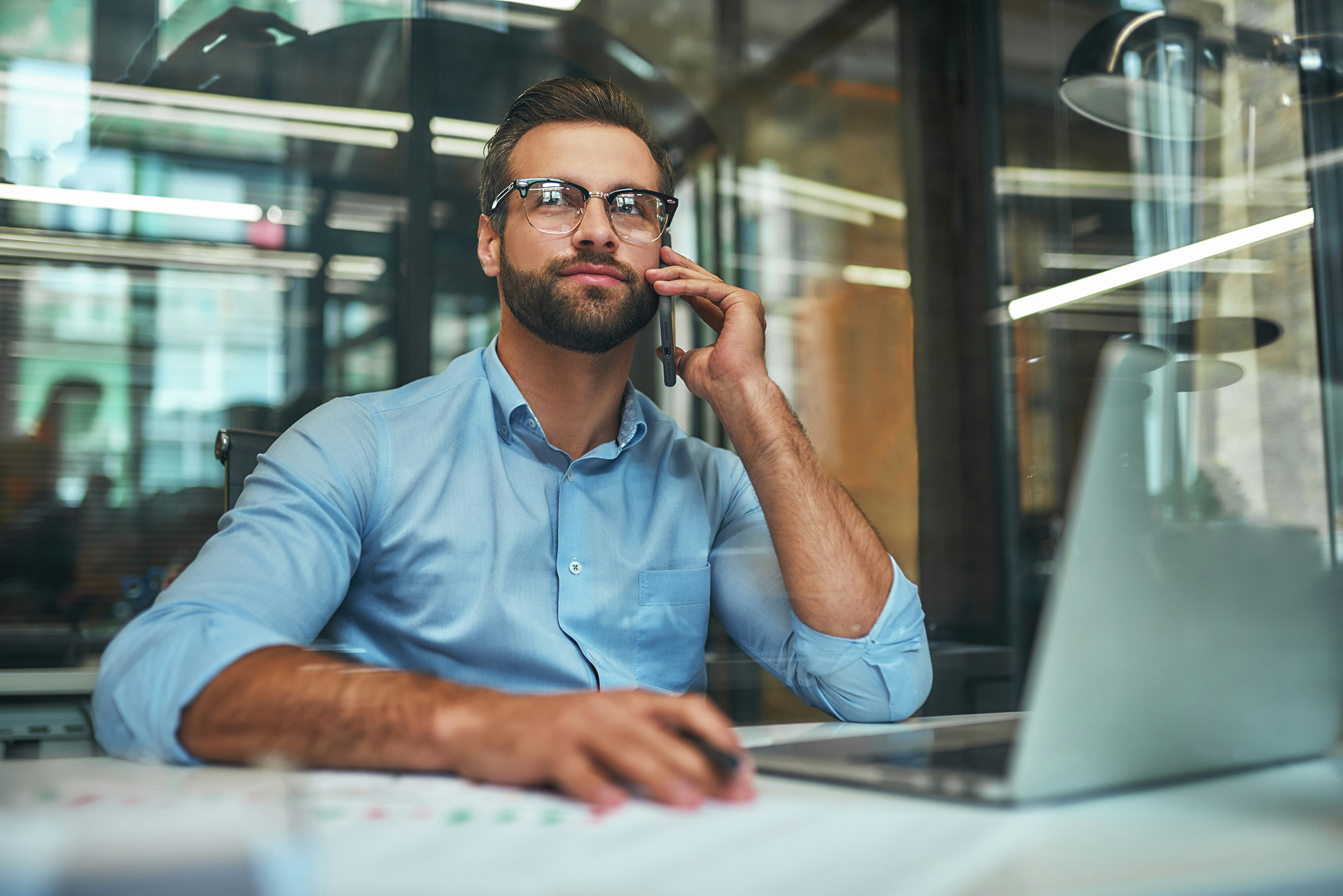 Mann sitzt am Schreibtisch vor Laptop mit Agentforce Service und telefoniert mit Handy.