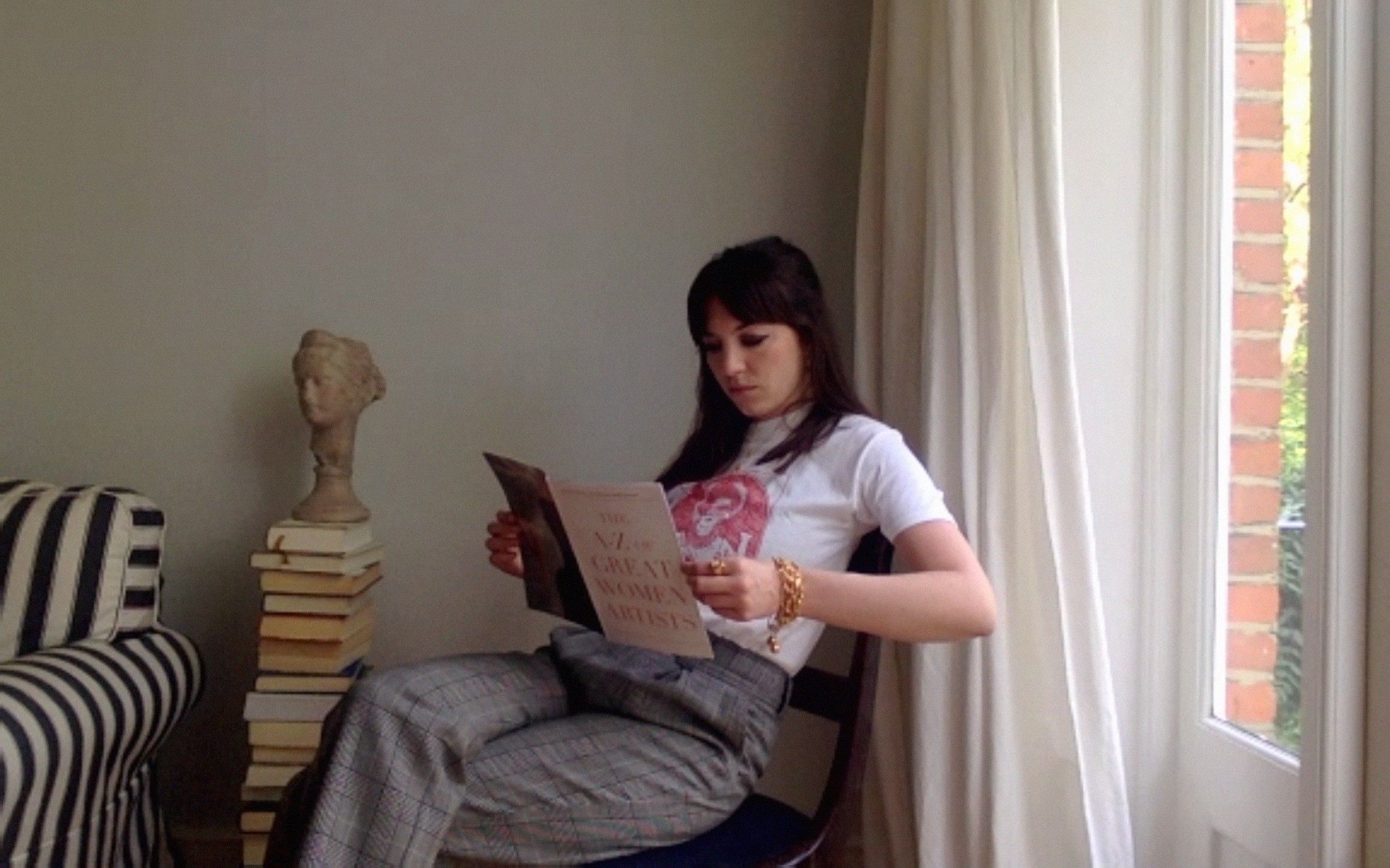 A woman with bangs reads a book titled 'The A-Z of Great Women Artists'.