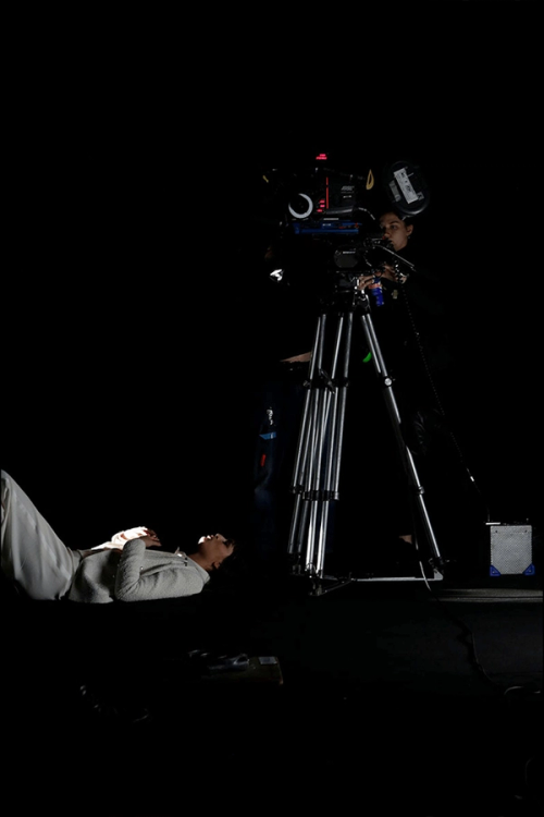 A cameraperson films a person lying on the floor in a dark studio.