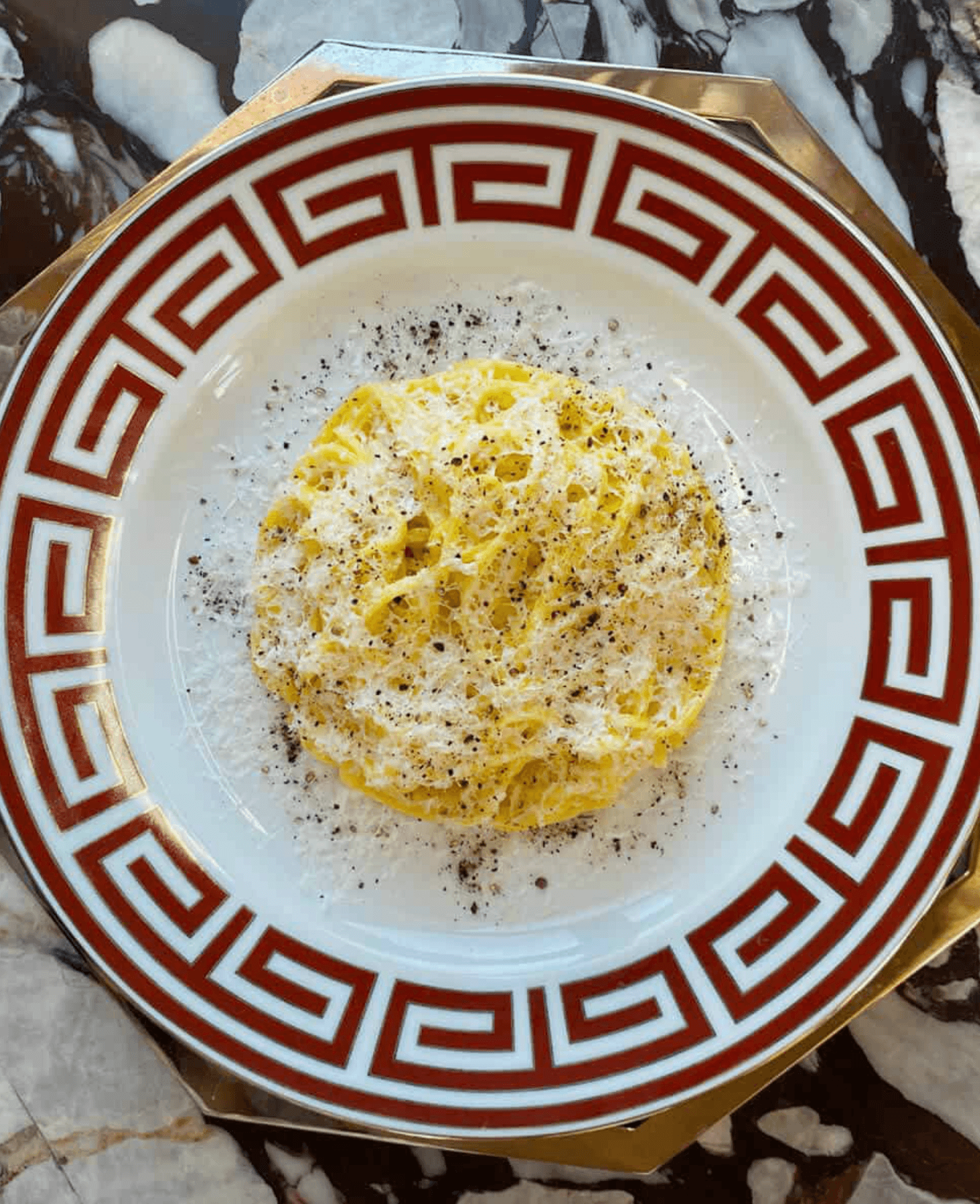 Spaghetti cacio e pepe on a white plate with a red Greek key border.