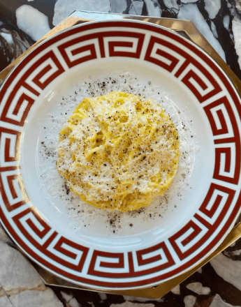 Cacio e Pepe pasta with grated cheese and black pepper on a white plate with a red Greek key pattern.