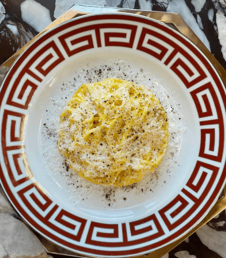 Spaghetti cacio e pepe on a white plate with a red Greek key border.
