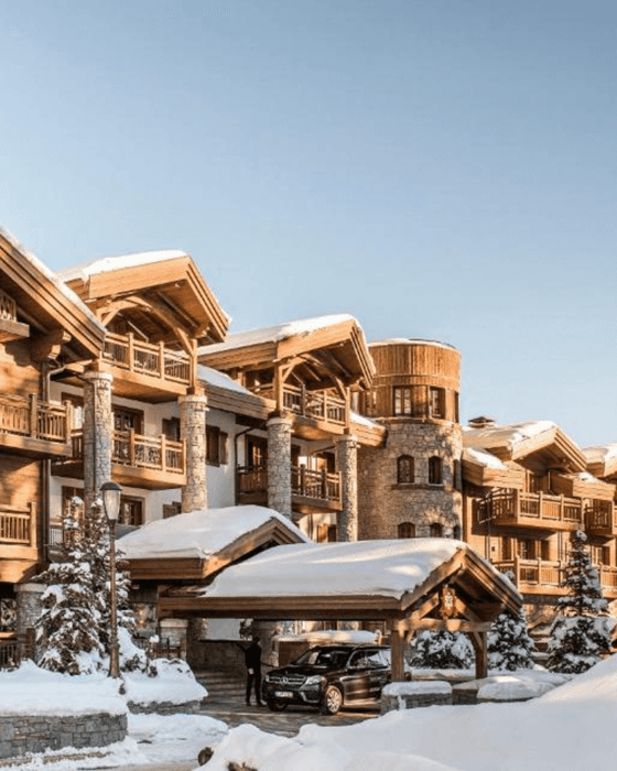Luxurious snow-covered chalet-style hotel with a car at its entrance.