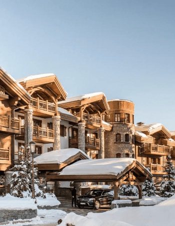 Luxurious snow-covered chalet-style hotel with a car at its entrance.