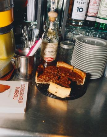 A pecan pie, a bottle of Ferrand cognac, stacked plates, and a book on a bar counter.