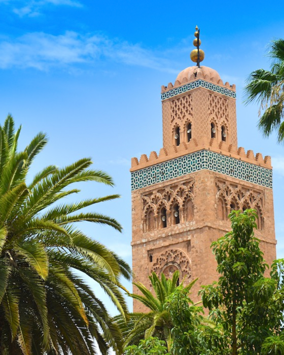 Koutoubia Minaret, an ornate terracotta tower with green tilework, surrounded by palm trees under a blue sky.