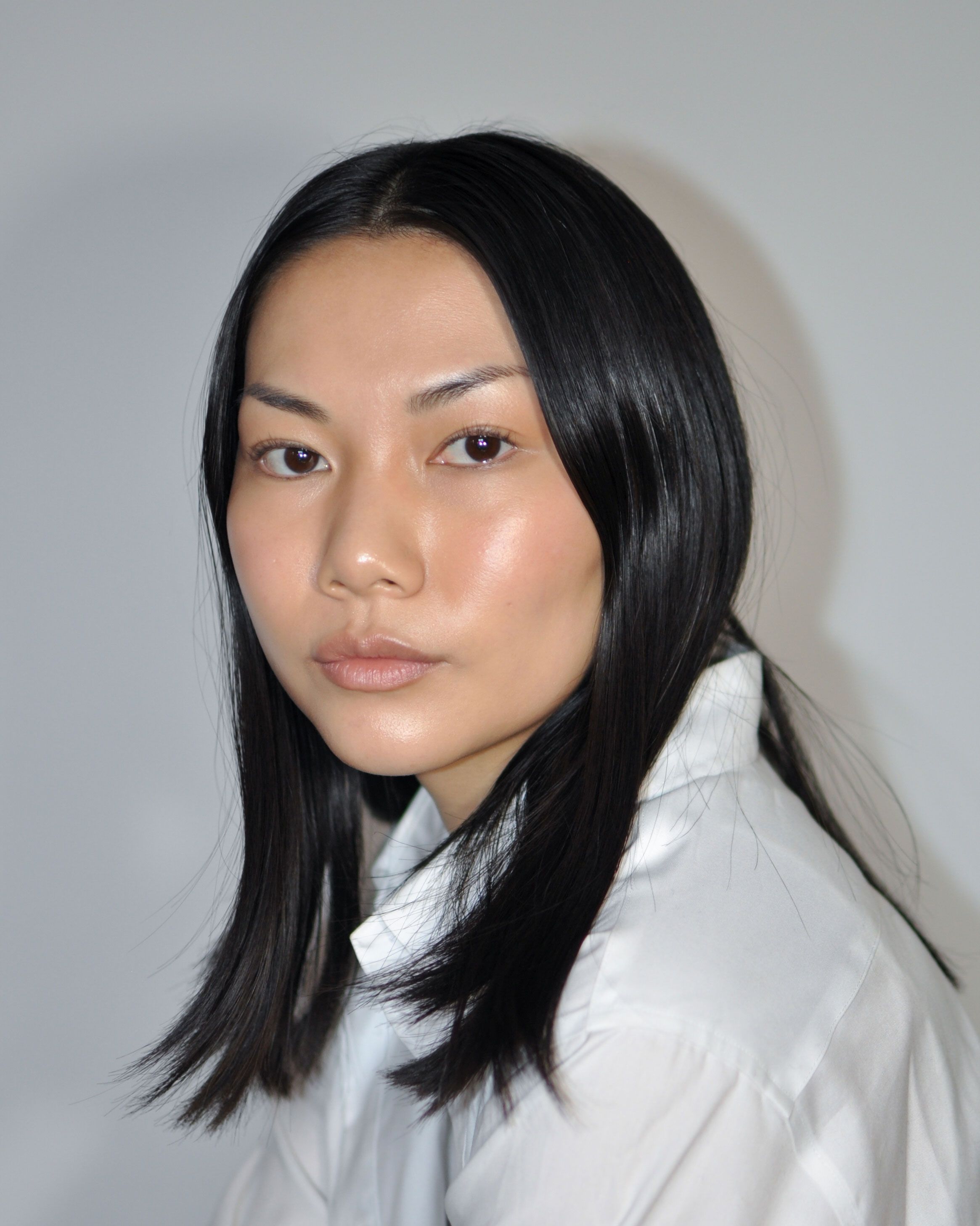 East Asian woman with long dark hair in a white shirt, looking at the camera.