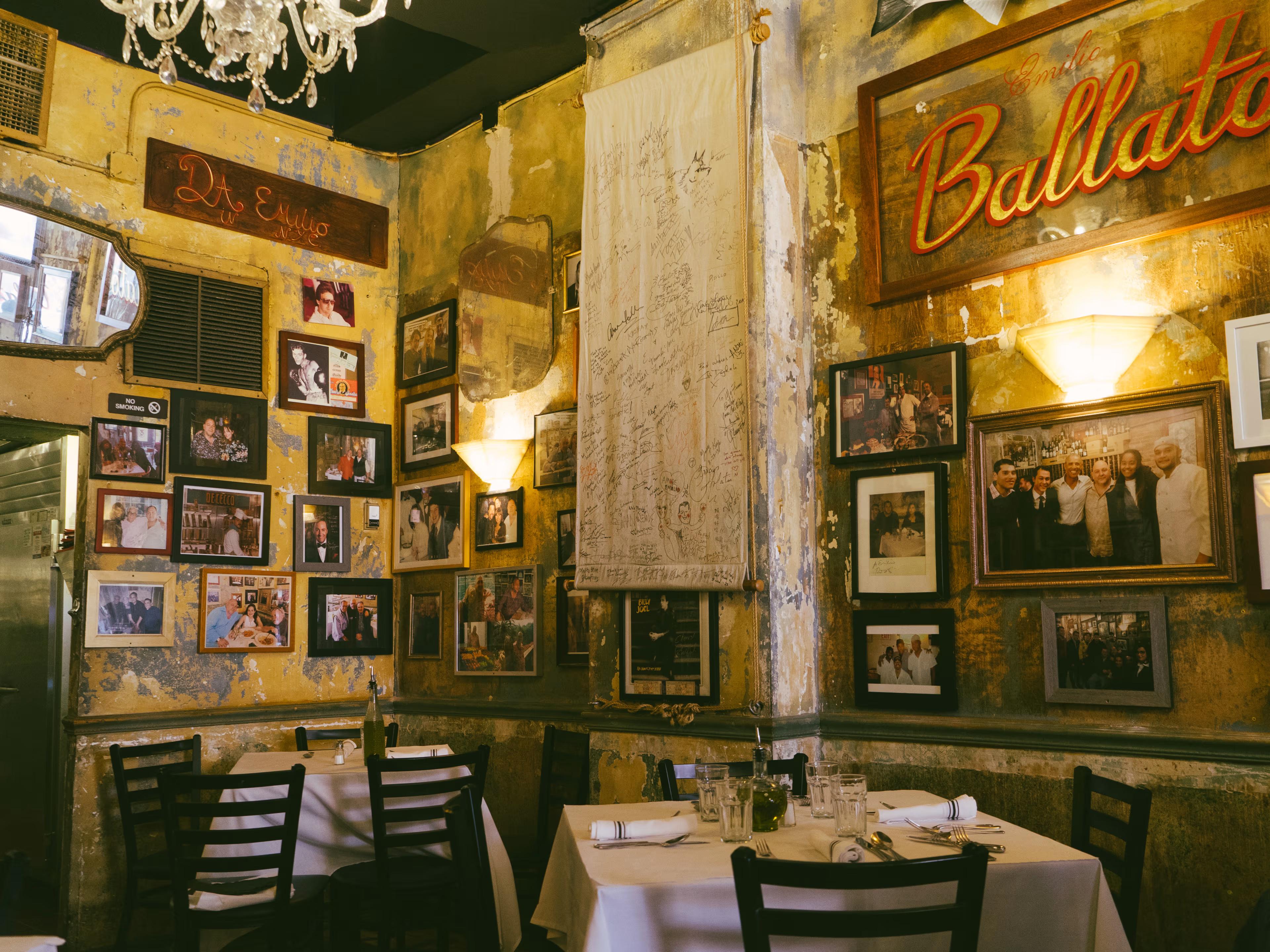 Rustic restaurant interior with yellow, peeling walls covered in framed photos and a signed banner, featuring set dining tables.