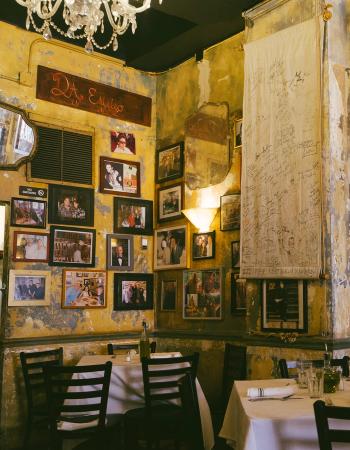 Rustic restaurant interior with yellow, peeling walls covered in framed photos and a signed banner, featuring set dining tables.