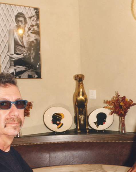 A man in sunglasses sits at a table while a woman in a chef's uniform stands beside him in a decorated room.