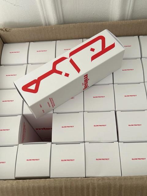 A cardboard box filled with white product boxes labeled "Glow Protect," with one larger white box featuring red Arabic script and "misaj" resting diagonally on top.