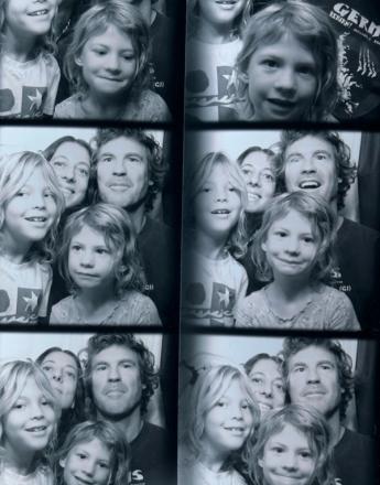 A black and white photo booth strip showing a family of four (two adults, two children) making various happy faces across multiple frames.