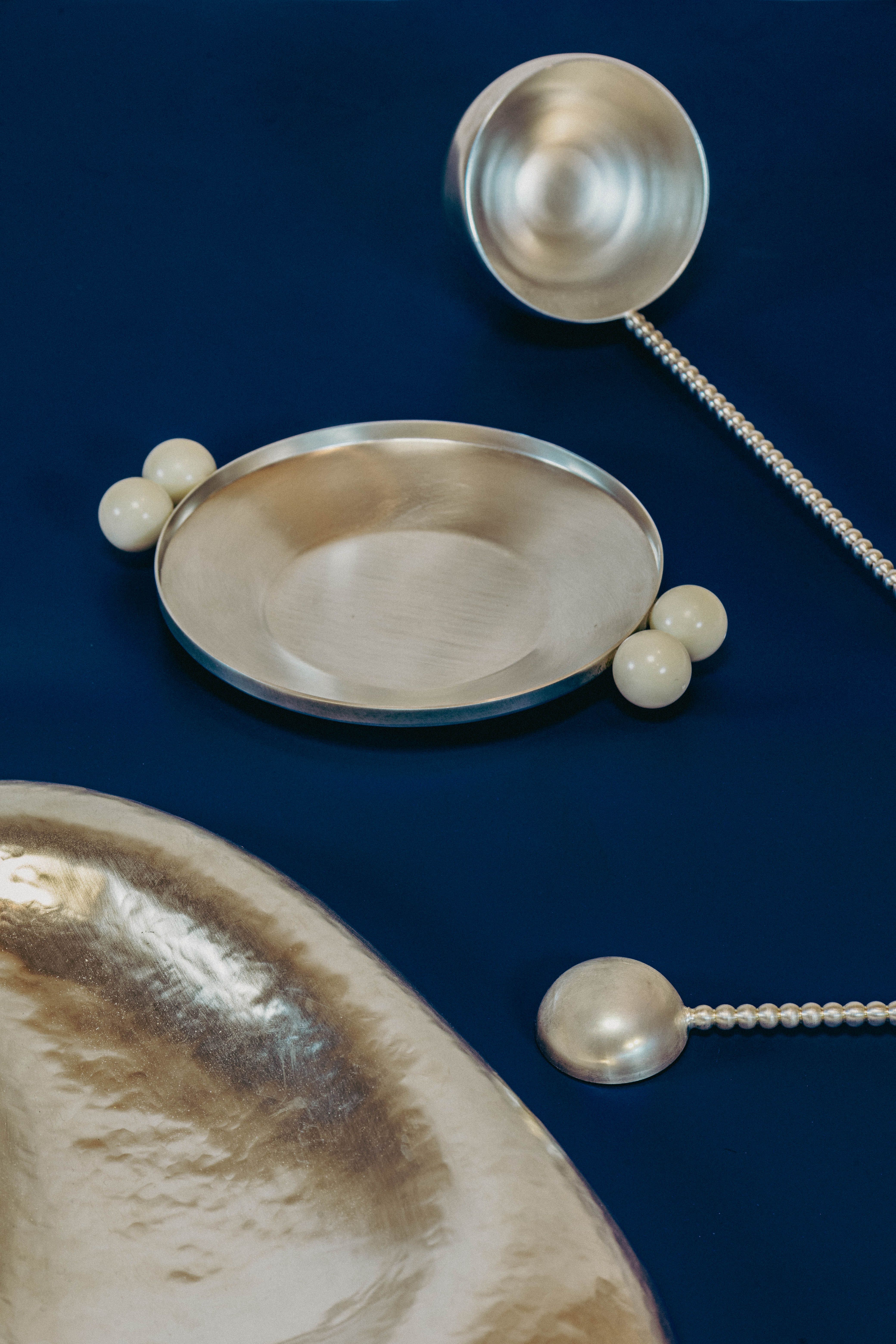 Silver dish, two ladles, and white spheres on a dark blue background. Made by Natalia Criado