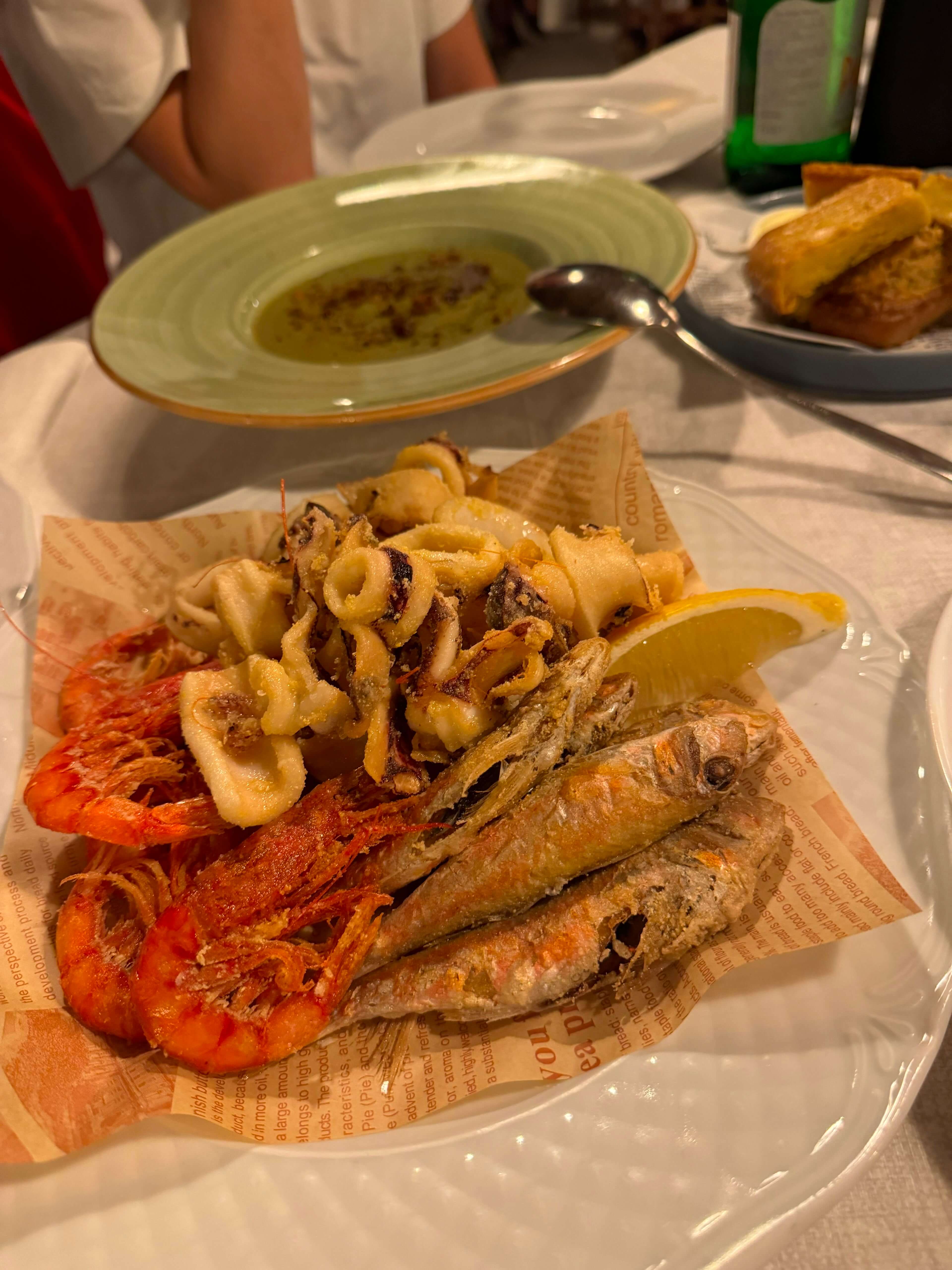 A plate of fried calamari, shrimp, and small fish with a lemon wedge.