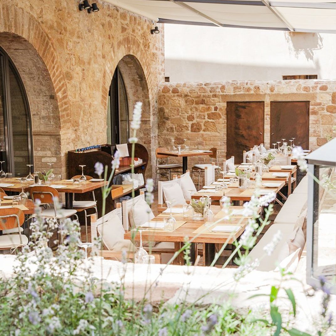 Outdoor restaurant patio with set wooden tables, stone walls, and lavender in the foreground.