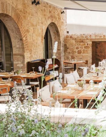 Outdoor restaurant patio with set wooden tables, stone walls, and lavender in the foreground.
