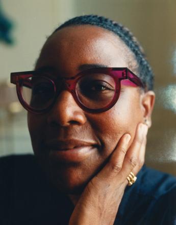 Mashama Bailey, Semaine Tastemaker. A smiling person with dark skin, wearing red glasses, rests a hand on their cheek.