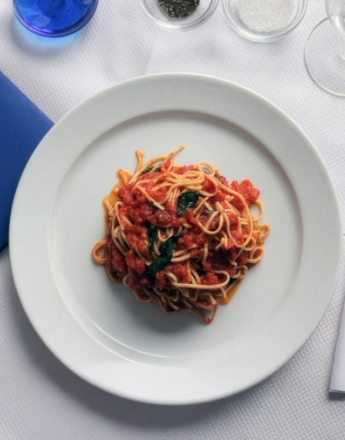 A plate of spaghetti with tomato sauce and basil on a white table setting.