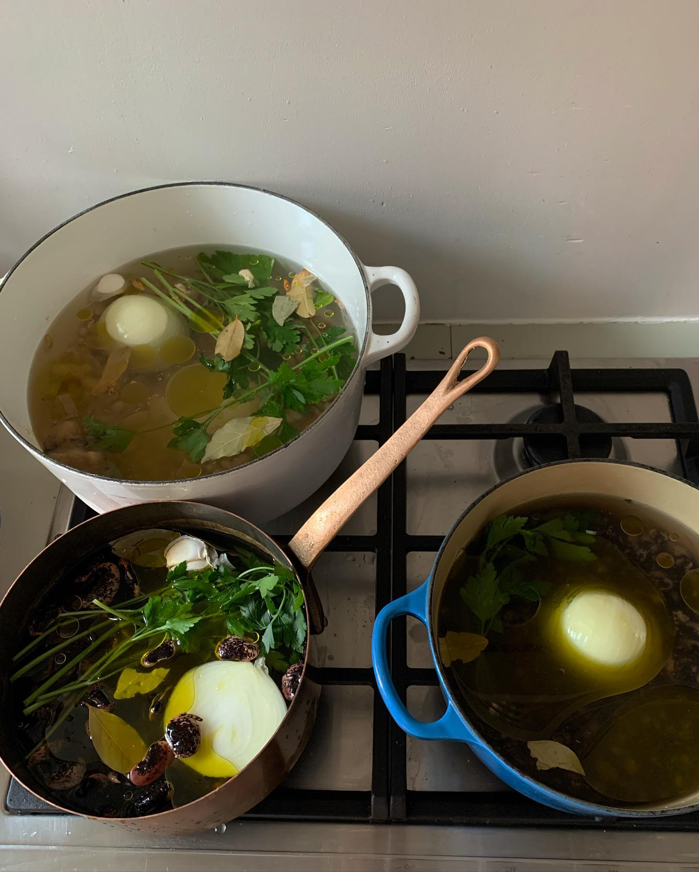 Three pots of stock with onions and herbs simmering on a stovetop.