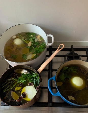 Three pots of stock with onions and herbs simmering on a stovetop.