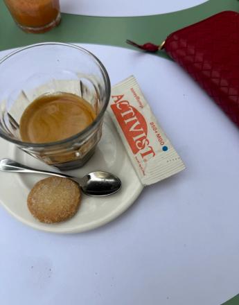 A glass of espresso with a cookie, spoon, and honey packet on a saucer next to a red wallet.
