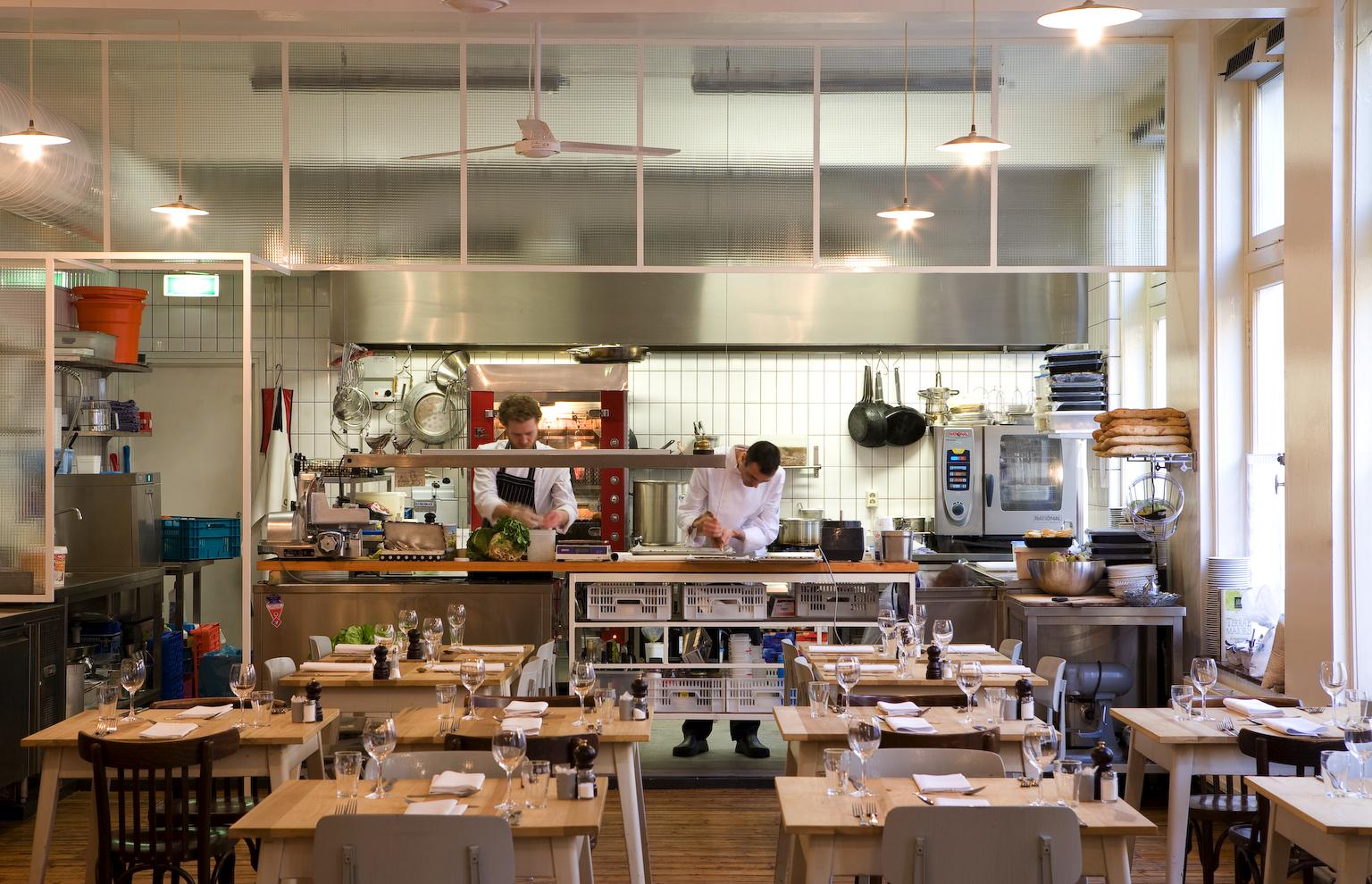 Restaurant with an open kitchen where chefs prepare food, and dining tables are set.
