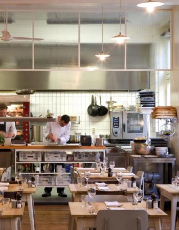 Restaurant with an open kitchen where chefs prepare food, and dining tables are set.