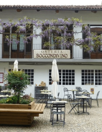 Outdoor patio of Osteria Boccondivino with wisteria vines, tables, chairs, and umbrellas.