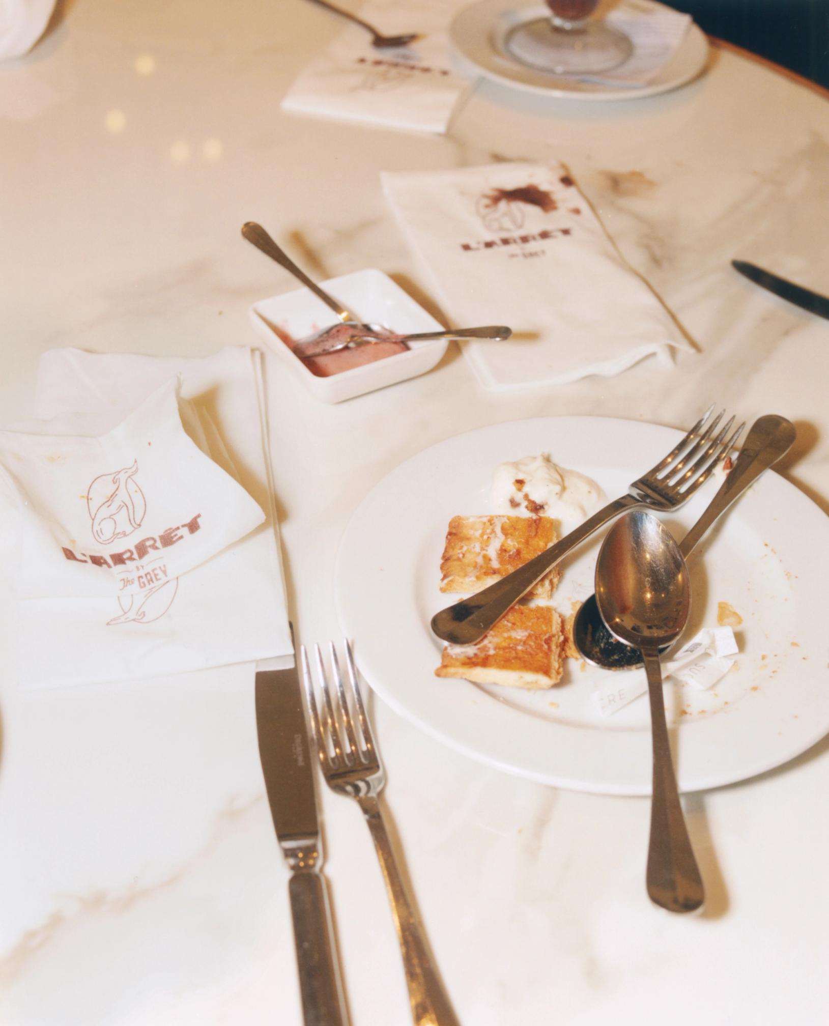A white marble table with remnants of a dessert, including pastries with ice cream, a small dish of jam, and crumpled napkins.
