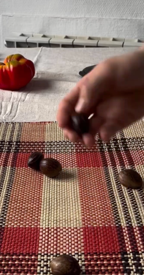 A hand holds a nutmeg over a patterned placemat with other nutmegs and a bell pepper nearby.