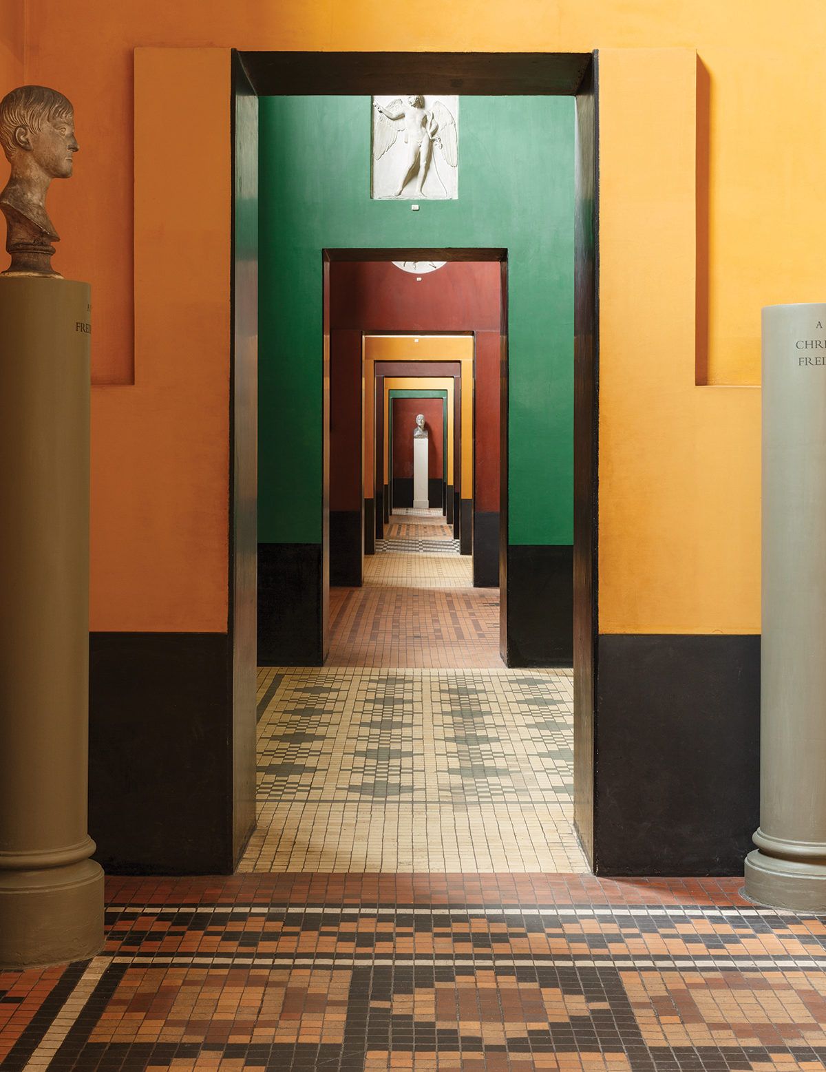 Colorful receding doorways in a museum hallway with sculptures and a patterned tile floor.