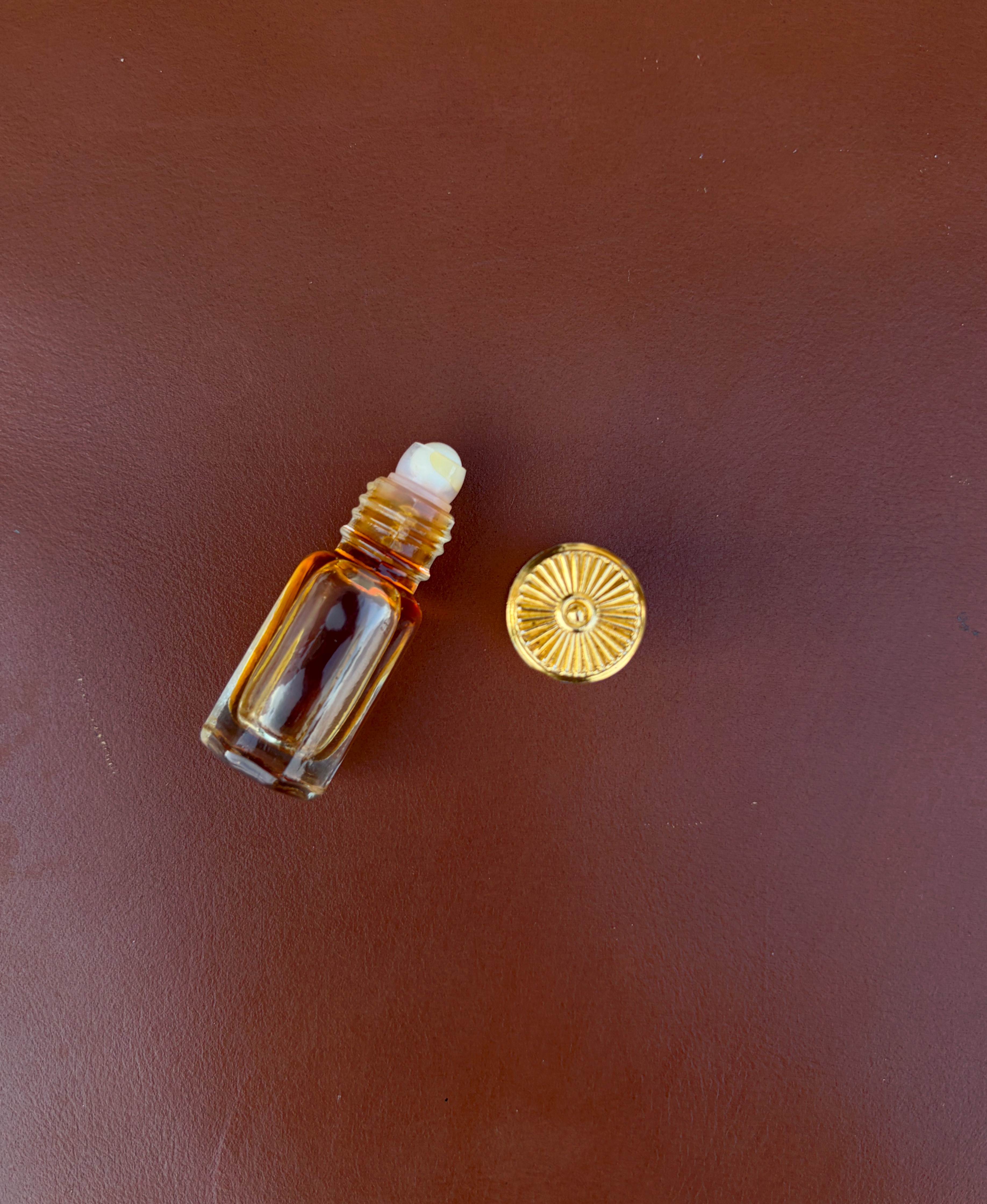 Amber roll-on perfume bottle with its golden cap beside it on a brown surface.