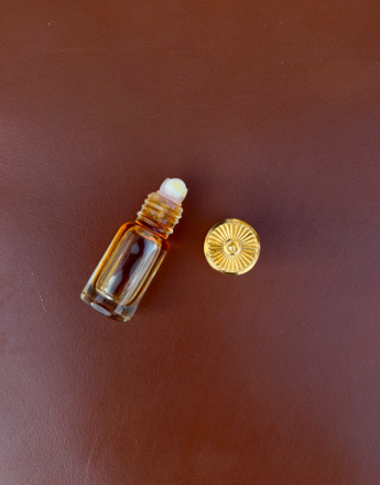 Amber roll-on perfume bottle with its golden cap beside it on a brown surface.