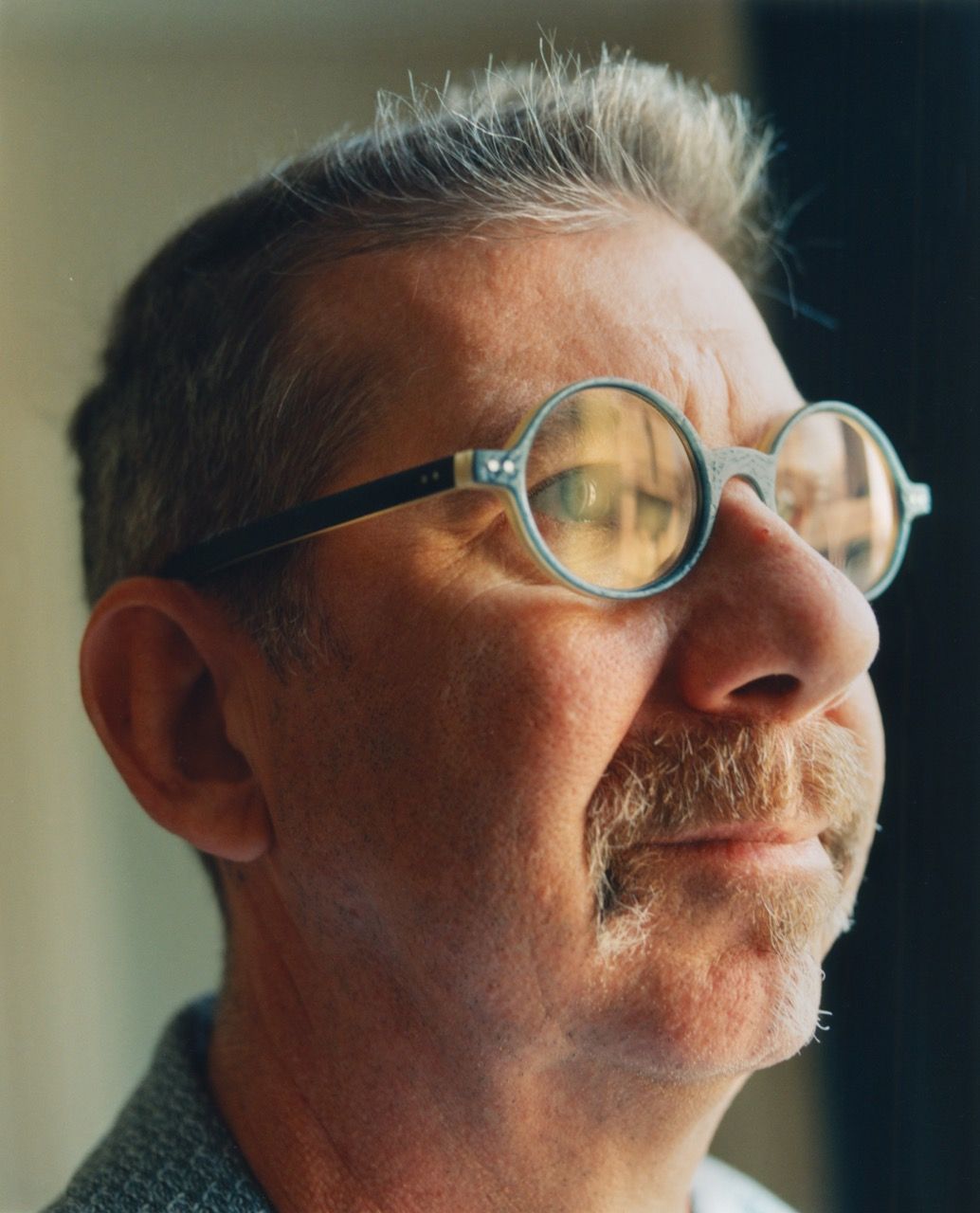 Close-up profile of a man with a mustache and gray hair wearing round glasses, looking upwards.