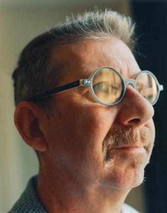 Close-up profile of a man with a mustache and gray hair wearing round glasses, looking upwards.