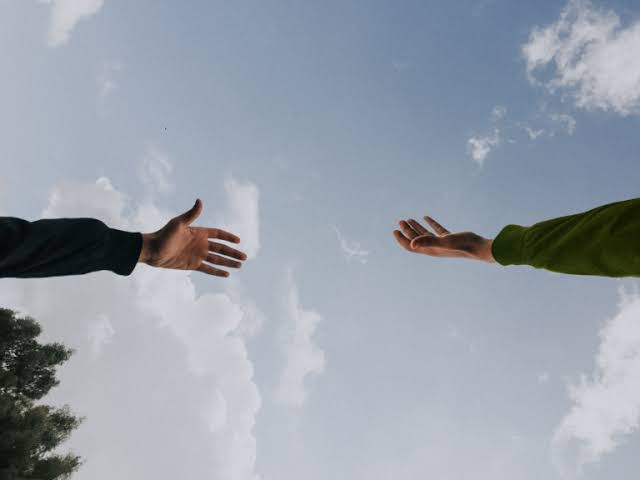Two hands extending towards each other against a blue sky with white clouds.