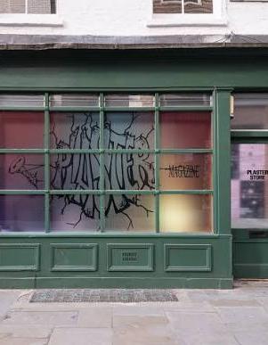 A dark green storefront with a large window displaying "PLASTER MAGAZINE" in black graffiti-style text over gradient colored panes, flanked by two green doors. The right door shows "PLASTER STORE" on a sign.