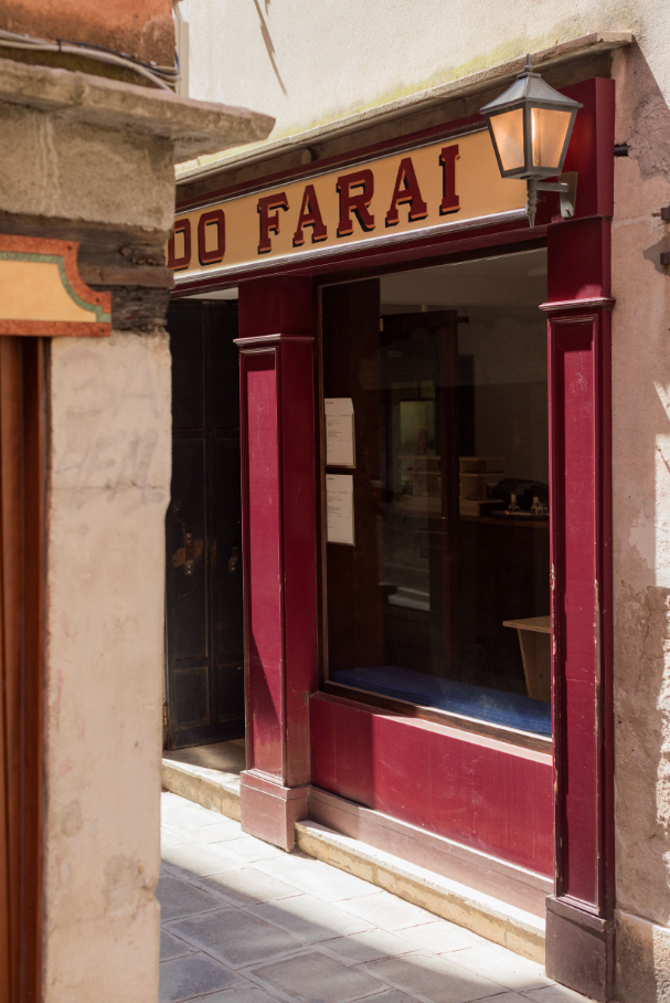 A shop entrance with a red frame, a sign reading 'DO FARAI', and a lit lamp on a narrow, sunny alley.
