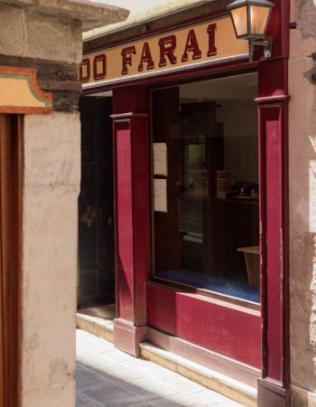 A shop entrance with a red frame, a sign reading 'DO FARAI', and a lit lamp on a narrow, sunny alley.