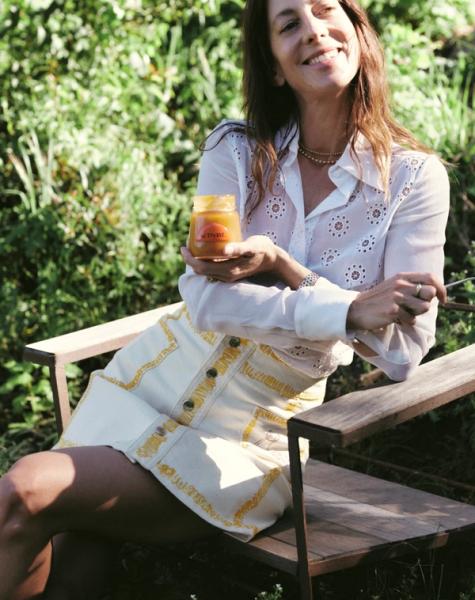A smiling woman sits outdoors, holding a jar of Activist honey.
