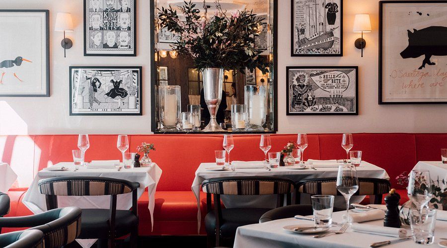 A vibrant restaurant interior with red booth seating, set tables with white tablecloths, and eclectic framed art on white walls.