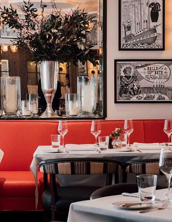 A vibrant restaurant interior with red booth seating, set tables with white tablecloths, and eclectic framed art on white walls.
