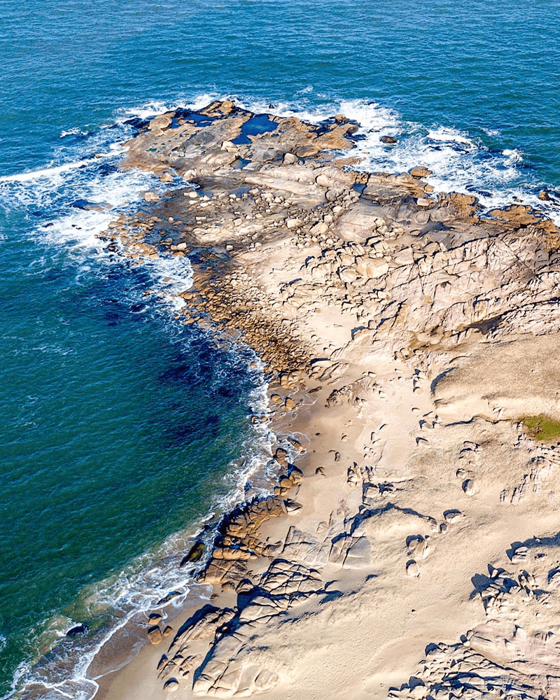 Aerial view of a rocky and sandy coastline with ocean waves.