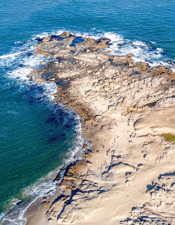 Aerial view of a rocky and sandy coastline with ocean waves.