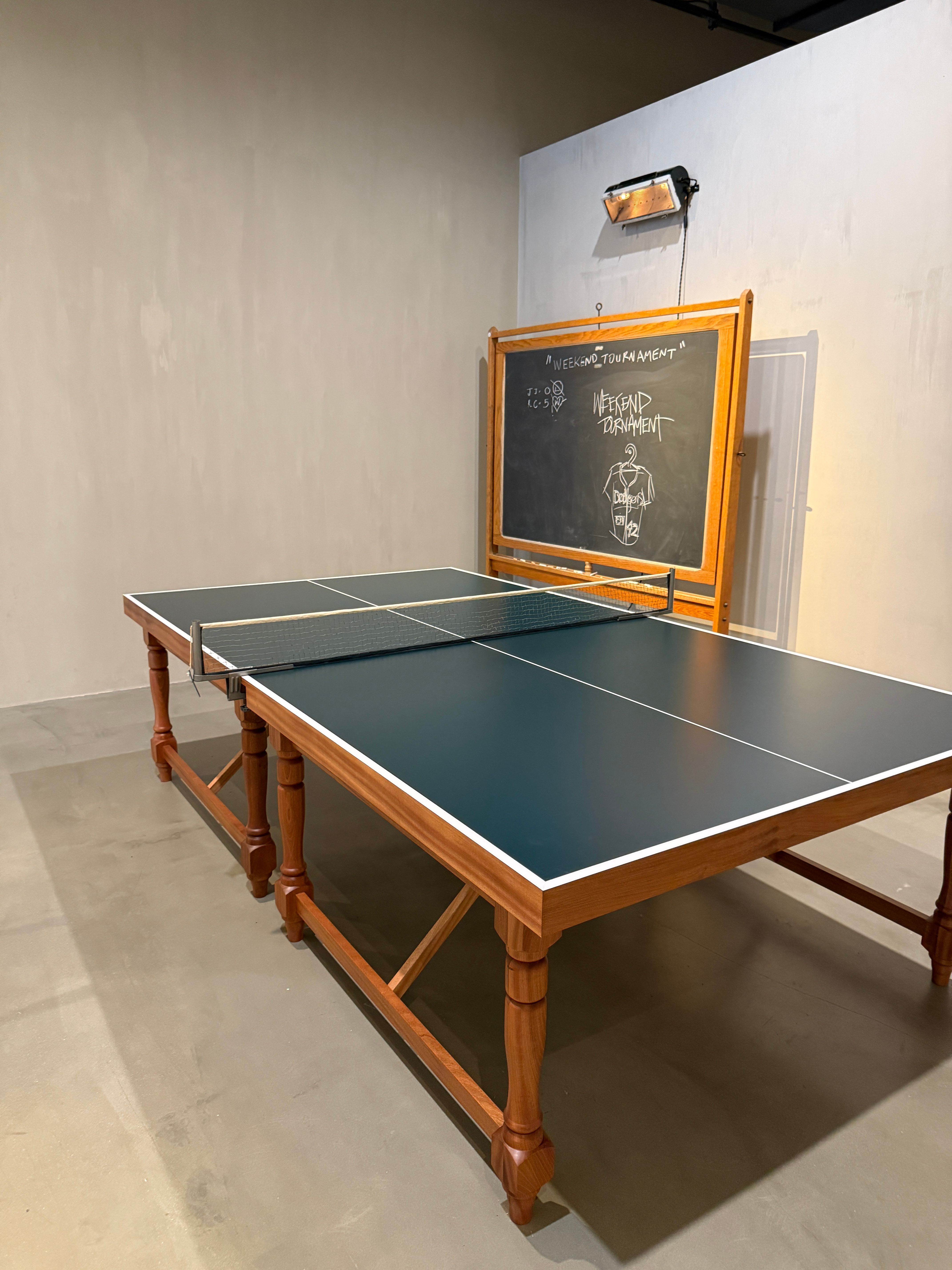 A dark green ping-pong table with a wooden frame in a room with a blackboard and a wall heater.